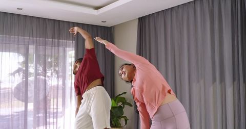 Diverse couple stretching together in sunlit living room wearing activewear for wellness