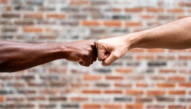 Two men fist-bumping forearms against brick wall conveying teamwork and unity