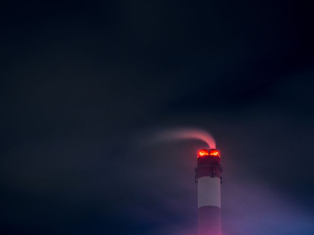 Industrial power station tower with smoke emitting into the dark night sky. Red lights on top create a dramatic effect. Ideal for use in topics related to energy production, industrial processes, pollution, and environmental impacts.