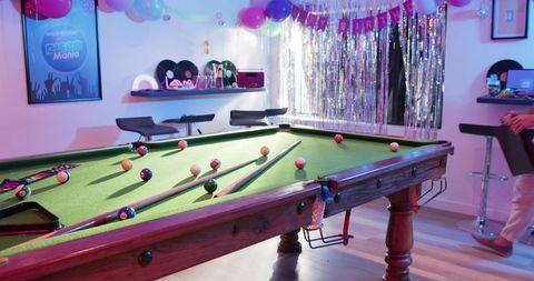 Friends playing pool at retro disco birthday party with neon lights and vinyl records