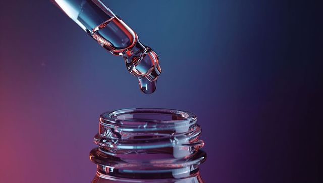 Droplet forming on pipette over bottle in gradient background