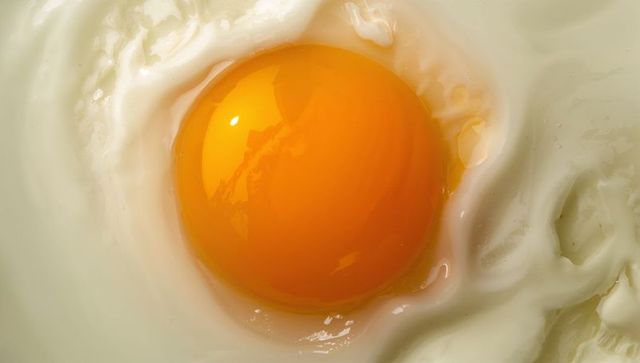 Glossy sunny-side-up egg yolk macro showcasing vibrant orange and creamy white curds