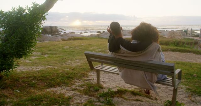Romantic diverse couple sitting on bench, embracing and looking at sunrise. Summer, vacation, romance, love, relationship, free time and lifestyle, unaltered.