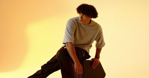 Stylish Young Man Sitting on Speaker in Warm Toned Studio
