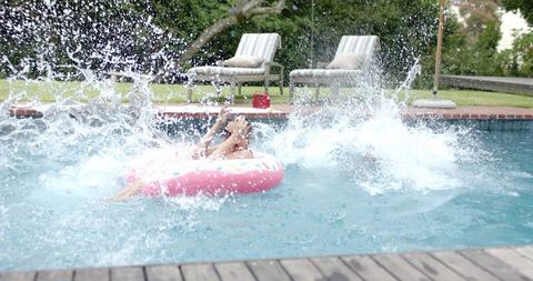 Woman relaxing on pink donut float while splashing in private backyard pool, summer leisure