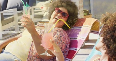 Sunlit friends relaxing on deck sipping pink cocktails on loungers with colorful towels