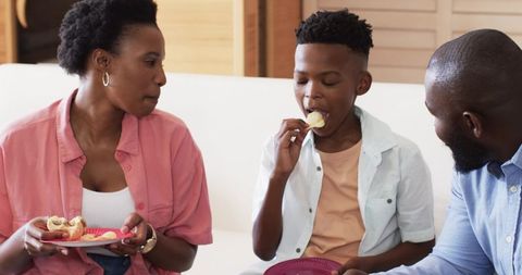 African American Family Sharing Snacks on Couch Laughing and Connecting, Casual Home Moment