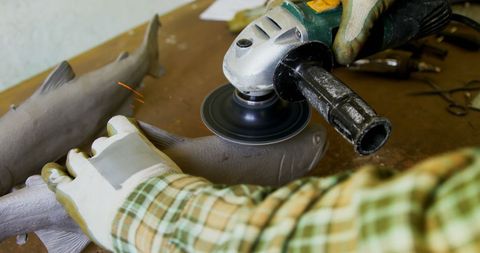 Person using angle grinder on wooden fish carving