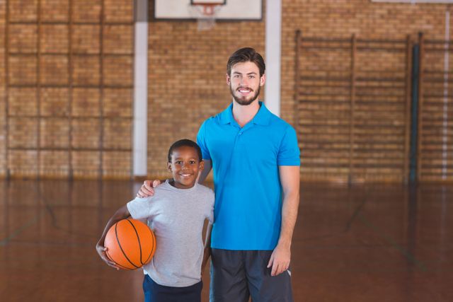 Portrait of sports teacher standing with his student in basketball court at school gym