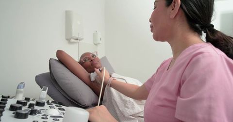 Clinician performing axillary ultrasound on african american woman during breast exam