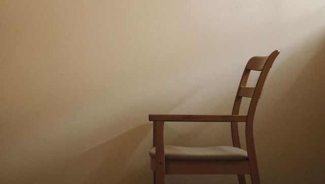 Minimalist Wooden Armchair Casting Diagonal Shadow on Neutral Beige Wall