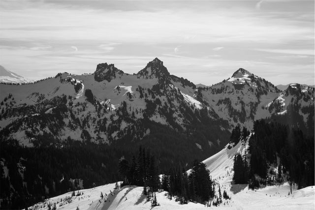 This image features snow-covered mountain peaks under a cloudy sky in a tranquil, black and white scene. It is ideal for use in travel blogs, websites focusing on winter activities, nature calendars, and outdoor adventure magazines. The monochromatic theme can also make it suitable for artistic collages or modern interior design decor.