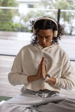 Non-binary adult meditating with headphones and smartwatch on deck for mindful practice