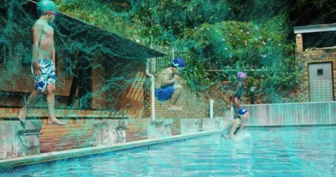 Boy jumping midair into pool in blue swim cap and trunks at sunny community pool