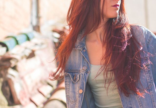 Fashion-conscious redhead woman outdoors wearing a denim jacket. Ideal for lifestyle blogs, fashion editorials, or promotional material emphasizing casual style and urban fashion.