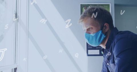 Data analyst wearing face mask leaning at window reviewing charts in sunlit office