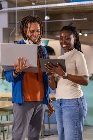 Smiling diverse coworkers collaborating with tablet and laptop in modern coworking space
