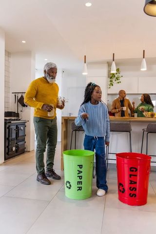 African american family recycling together in modern kitchen with paper and glass bins