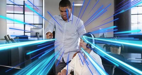 Mentor pointing at monitor guiding headset-wearing colleague through modern office tech