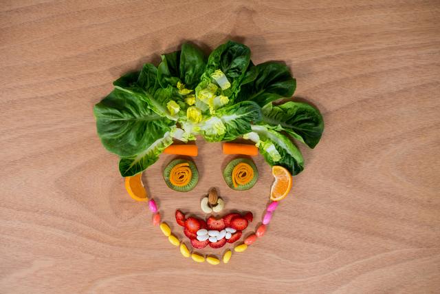 Creative arrangement of various vegetables and sweets forming a smiley face on a wooden surface. Useful for promoting healthy eating habits, children's nutrition, food creativity, and engaging content for food blogs or educational materials.