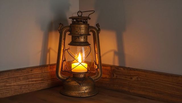Antique brass lantern with patina and pillar candle casting warm amber glow in rustic corner