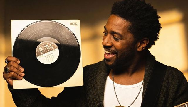 Man holding vintage vinyl record, smiling and admiring music in warm sunlight