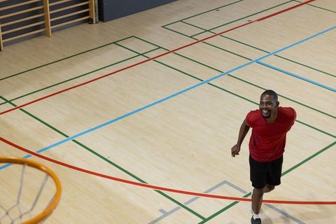 Smiling african american athlete running on indoor gym court near basketball hoop