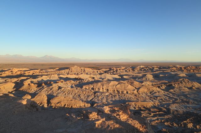 Panoramic view of an expansive desert landscape during sunset, highlighting the rocky and arid terrain. Ideal for use in travel, nature, or geology-related content. Perfect for illustrating themes of solitude, natural beauty, and the magnificence of untouched wilderness.