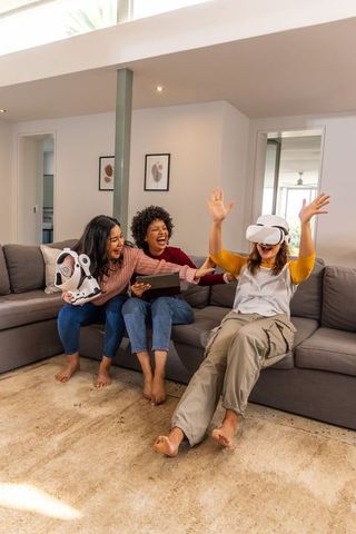 Friends enjoying virtual reality game on sectional sofa with tablet and toy robot