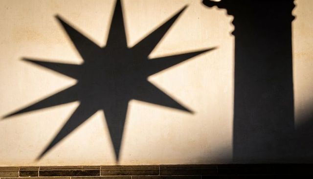 Eight-point star shadow casting on sunlit plaster wall with column silhouette