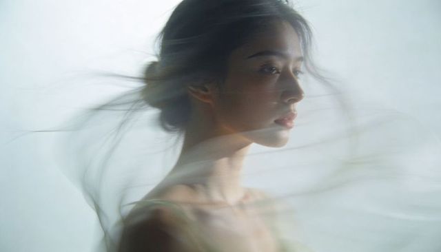 Gazing asian woman draped in sheer veil, ethereal soft-focus motion portrait