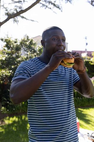 Young Man Eating Burger in Sunny Outdoor Garden Scene
