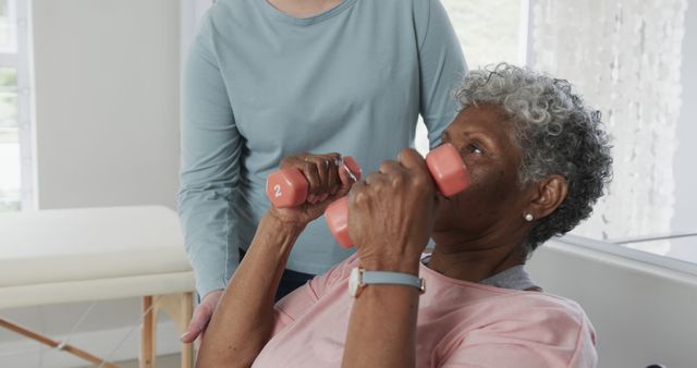 Older woman lifting dumbbells with physical therapist assistance. Ideal for content on senior healthcare, fitness routines for the elderly, rehabilitation exercises, physical therapy programs, and promoting healthy aging.