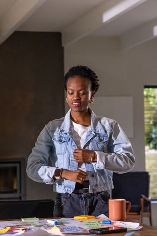 African american woman adjusting denim jacket in home workspace brainstorming with notes