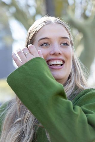 Young woman laughing and smiling outdoors wearing green coat backlit close-up portrait