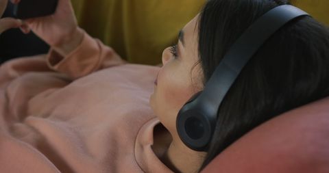 Relaxed Woman Enjoying Music on Sofa Using Smartphone