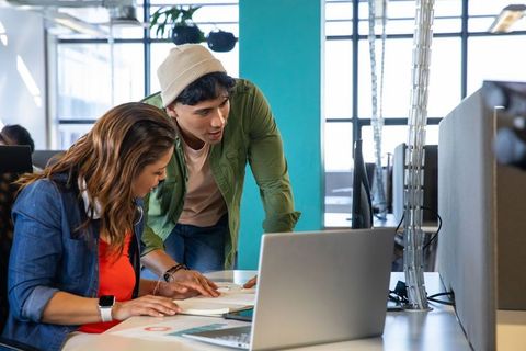 Coworkers collaborating and reviewing laptop documents in bright open-plan workspace