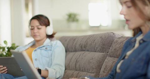 Friends relaxing on cozy gray sofa using tablet and headphones for streaming and study