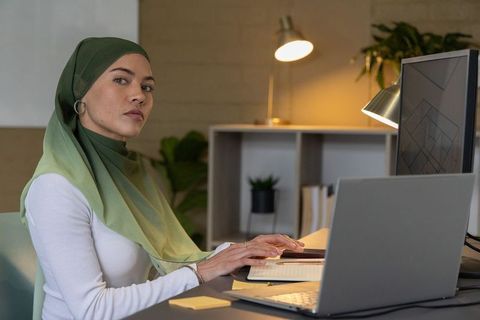 Focused professional wearing green ombre hijab working at minimalist desk with laptop