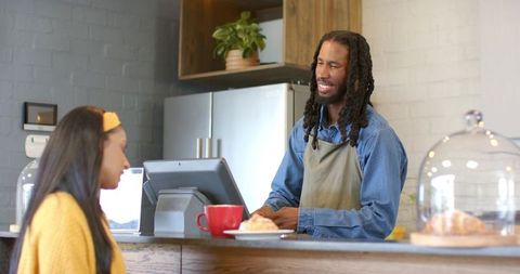 African american barista serving customer at cafe counter with pos terminal and pastry