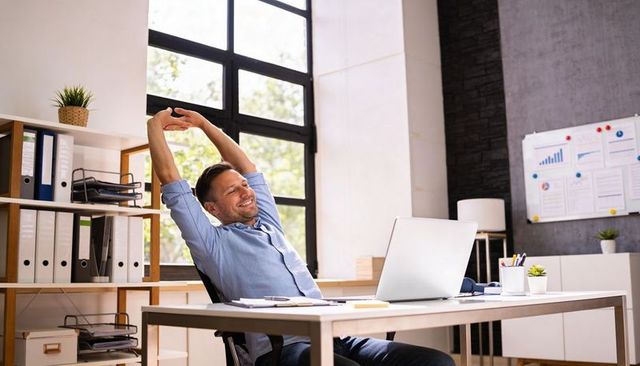 Man stretching at modern desk in sunlit office workspace boosting productivity