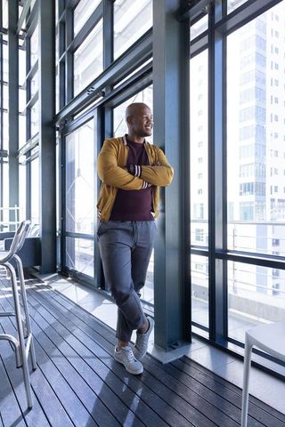 African american man leaning on column, looking at city through glass in modern atrium