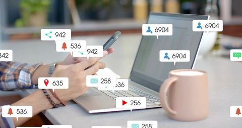 Hands tapping smartphone over laptop showing social media notifications and alerts