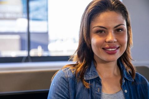 Smiling woman sitting in lounge wearing denim jacket and waiting by window, relaxed natural portrait