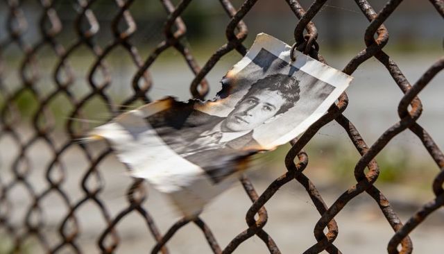 Flapping torn portrait snagging on rusted chain-link fence with charred edges urban decay