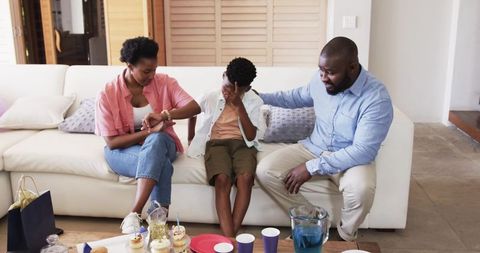 African american parents comforting upset child on couch during birthday celebration