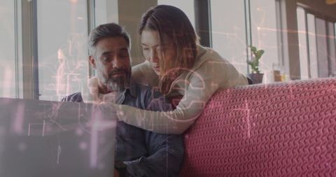 Couple collaborating on laptop on cozy pink sofa with digital interface overlay