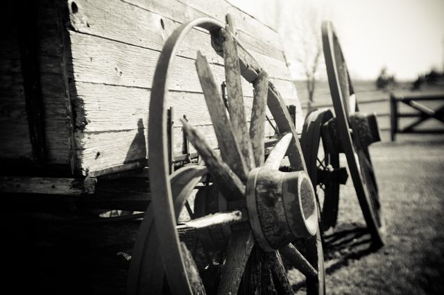 Close-up shows aged wooden wagon wheel in sepia tone. Useful for themes of history, rural life, antique vehicles, or farming. Perfect for posters, educational materials, websites on historical transportation, or rustic decor.