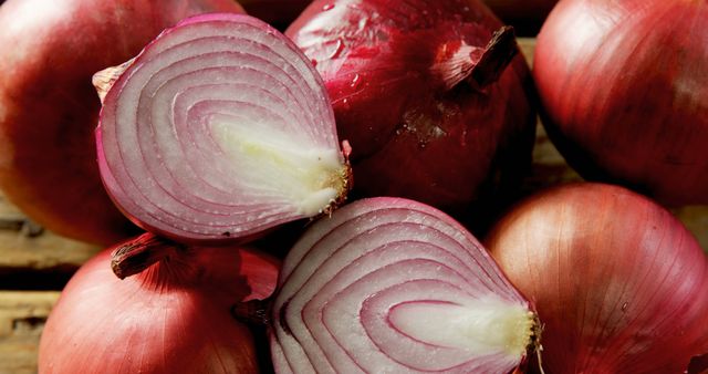 Red onions are arranged on a wooden surface, one cut in half to reveal its layers, with copy space. Red onions are a staple in culinary arts, valued for their vibrant color and distinctive flavor.