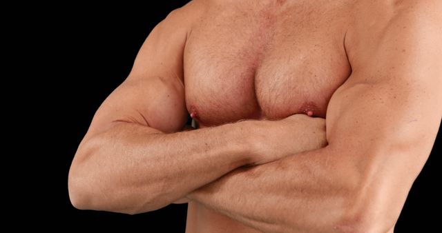 This stock photo shows a close-up of a fit male torso with arms crossed, emphasizing muscular definition. Ideal for use in fitness magazines, bodybuilding blogs, gym advertisements, and health and wellness campaigns.